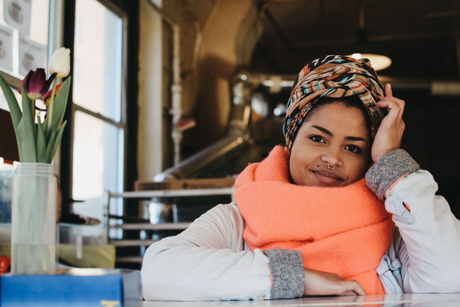 Person relaxing with bright orange scarf and headwrap in casual indoor setting.