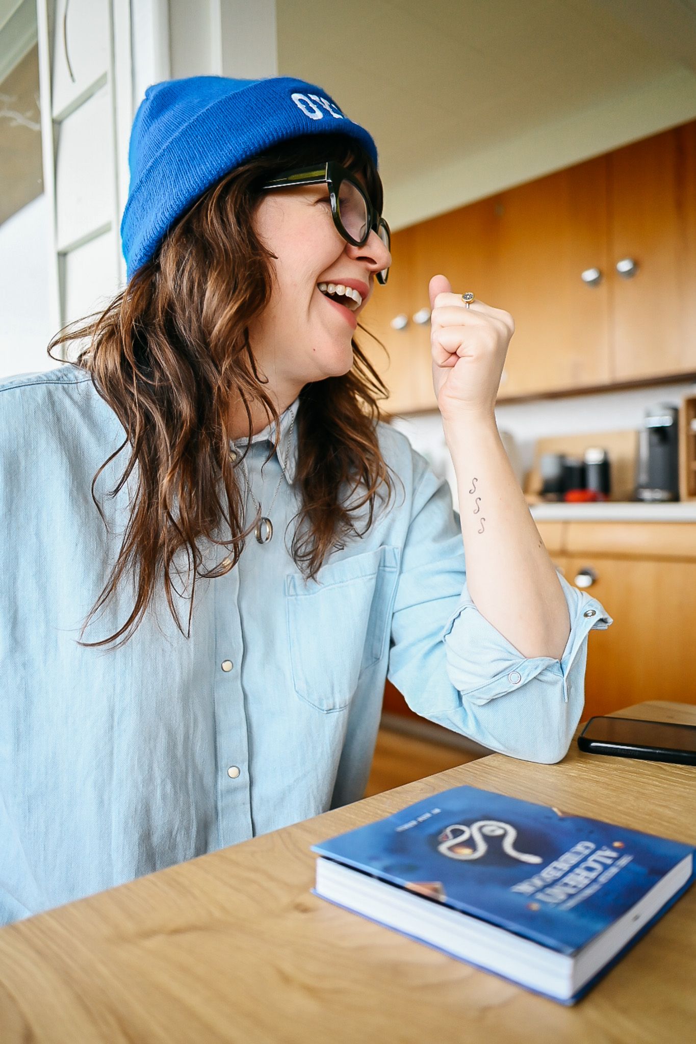 Person in blue cap and denim shirt expressing excitement while studying at wooden desk.