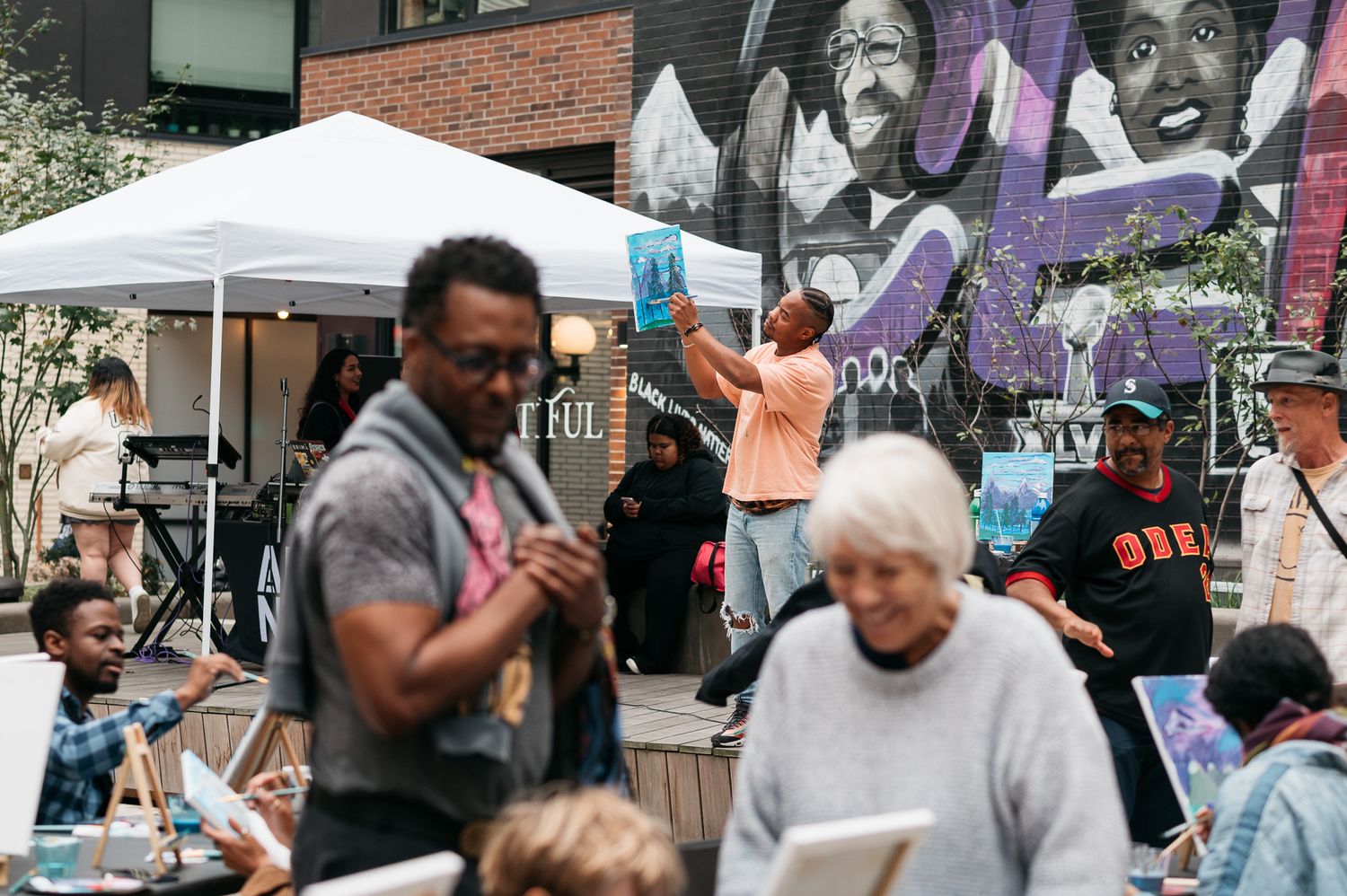 A diverse group of people gather at what appears to be a community or protest event with signs and banners visible.