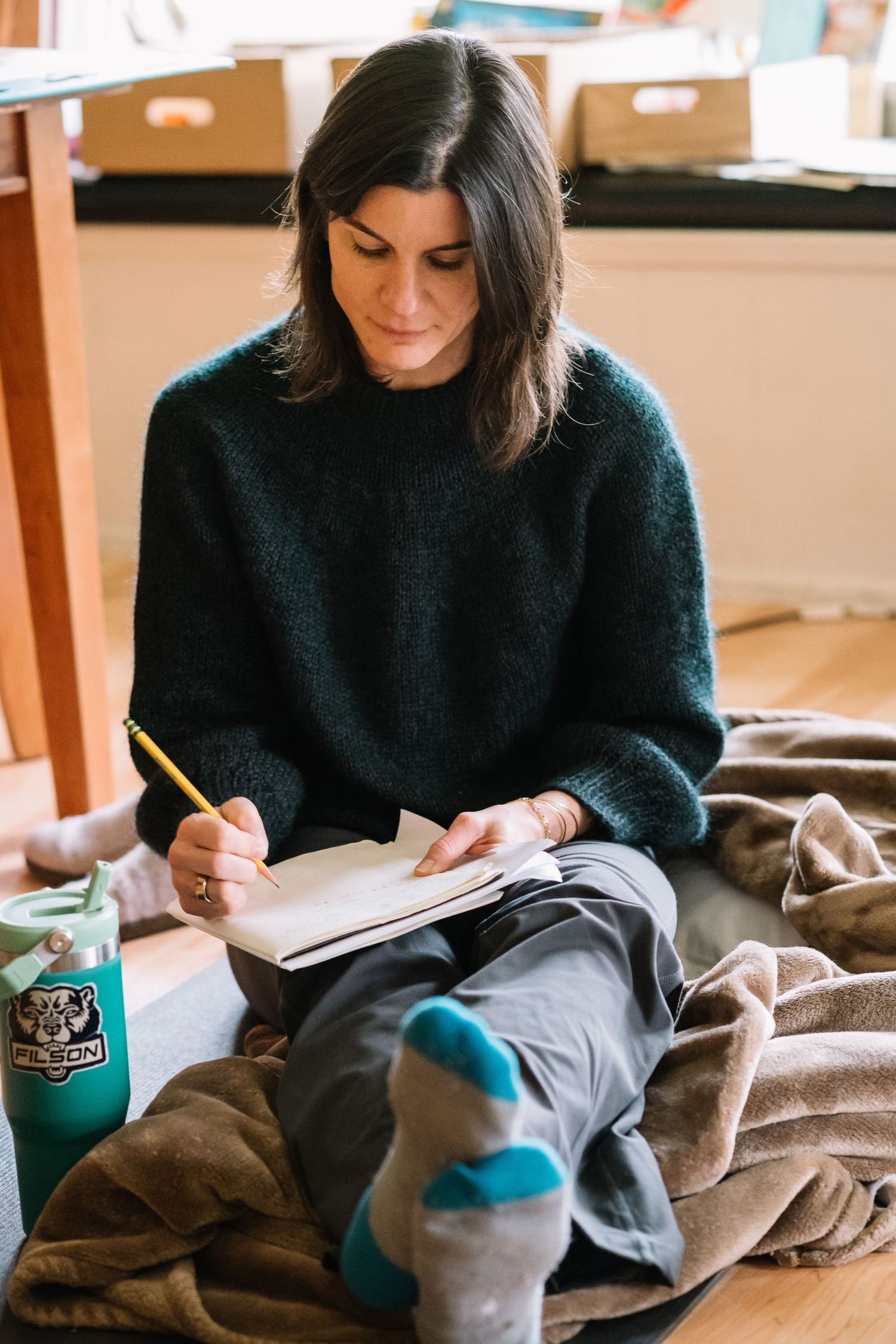 Person in black sweater writing in notebook while relaxing on cozy blanket.
