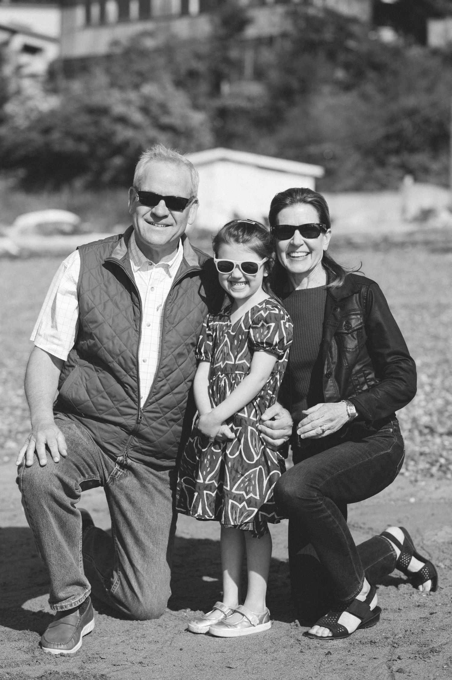 Group photo of people crouching together on a beach wearing sunglasses.