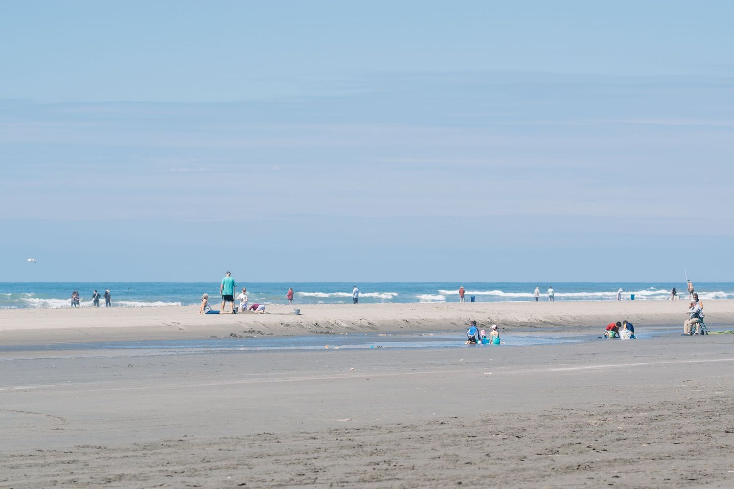 A wide view of a sandy beach with scattered beachgoers and ocean waves in the distance.