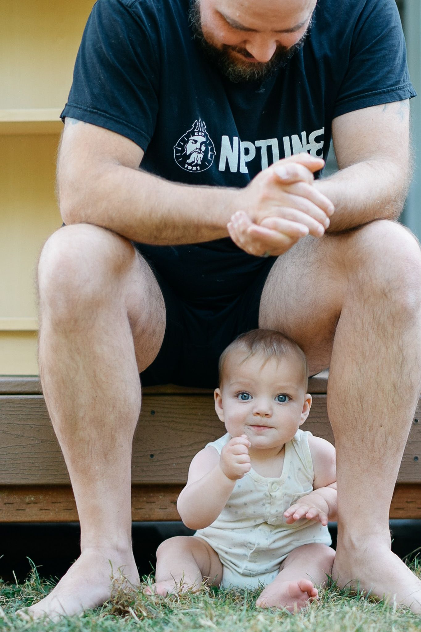 Parent and baby sitting together on grass in casual outdoor setting.