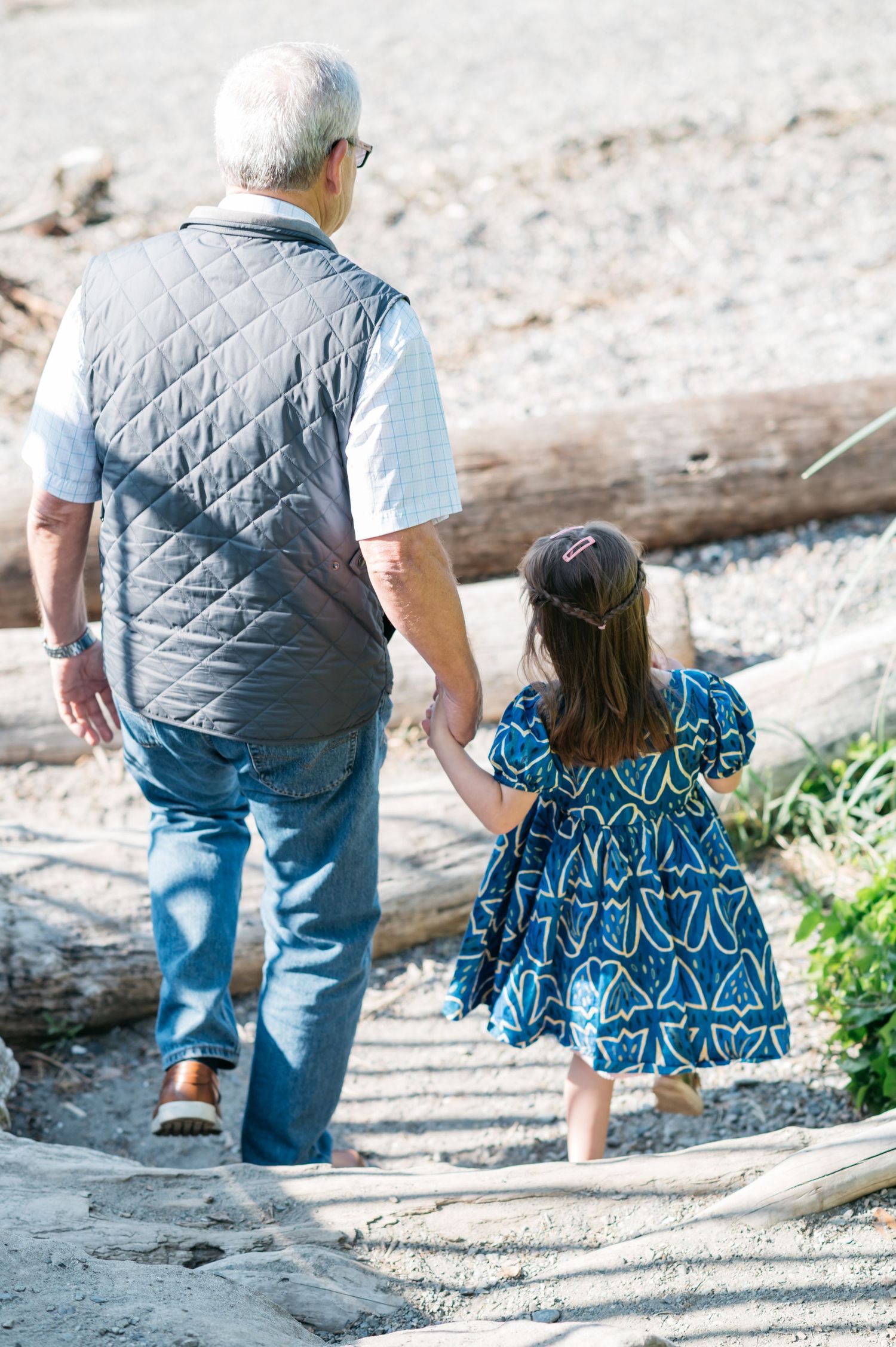A child in a blue patterned dress walks with adults on a rocky beach path.