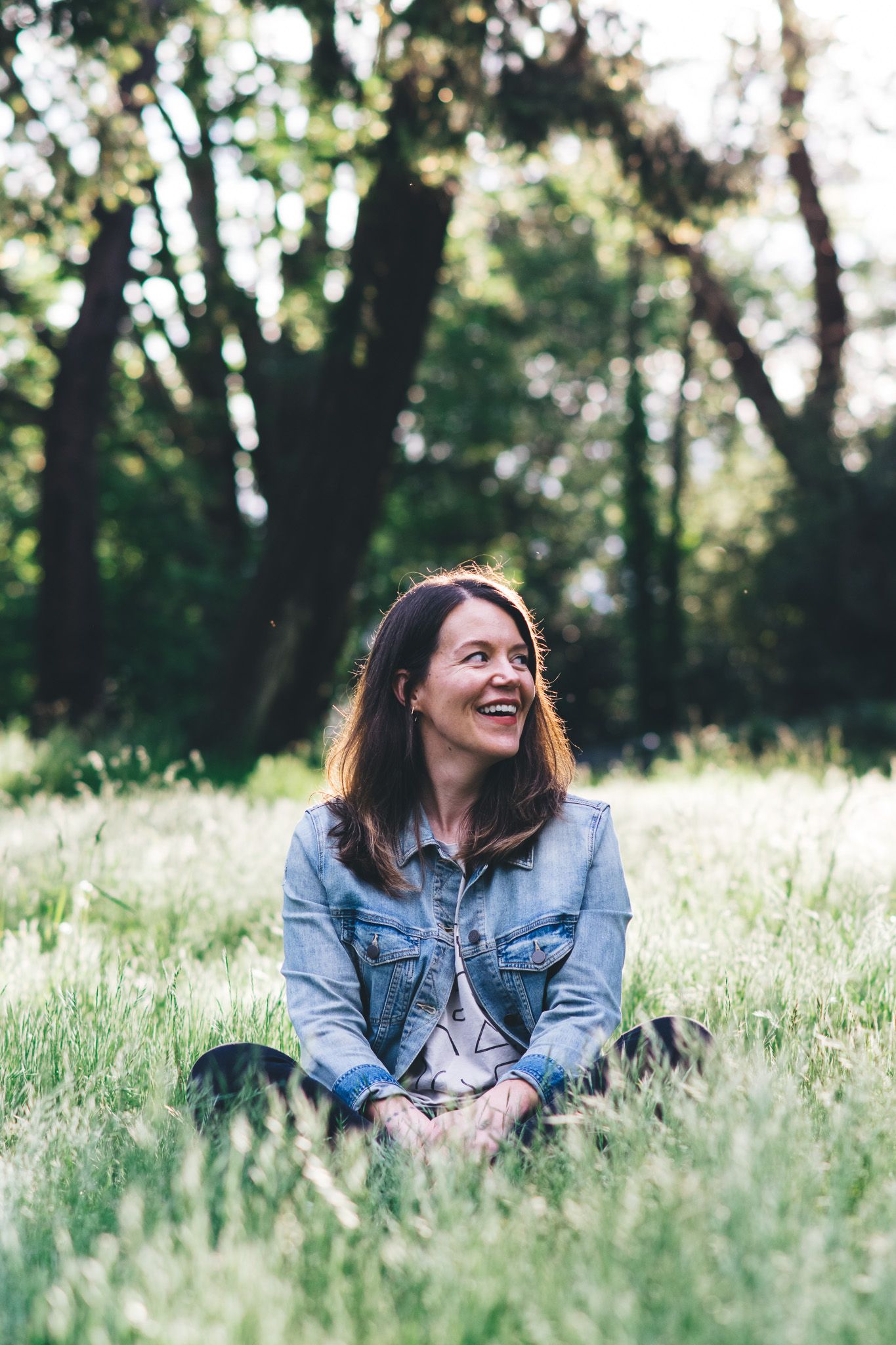 Candid portraits in a sunlit meadow with tall grass and denim jacket.