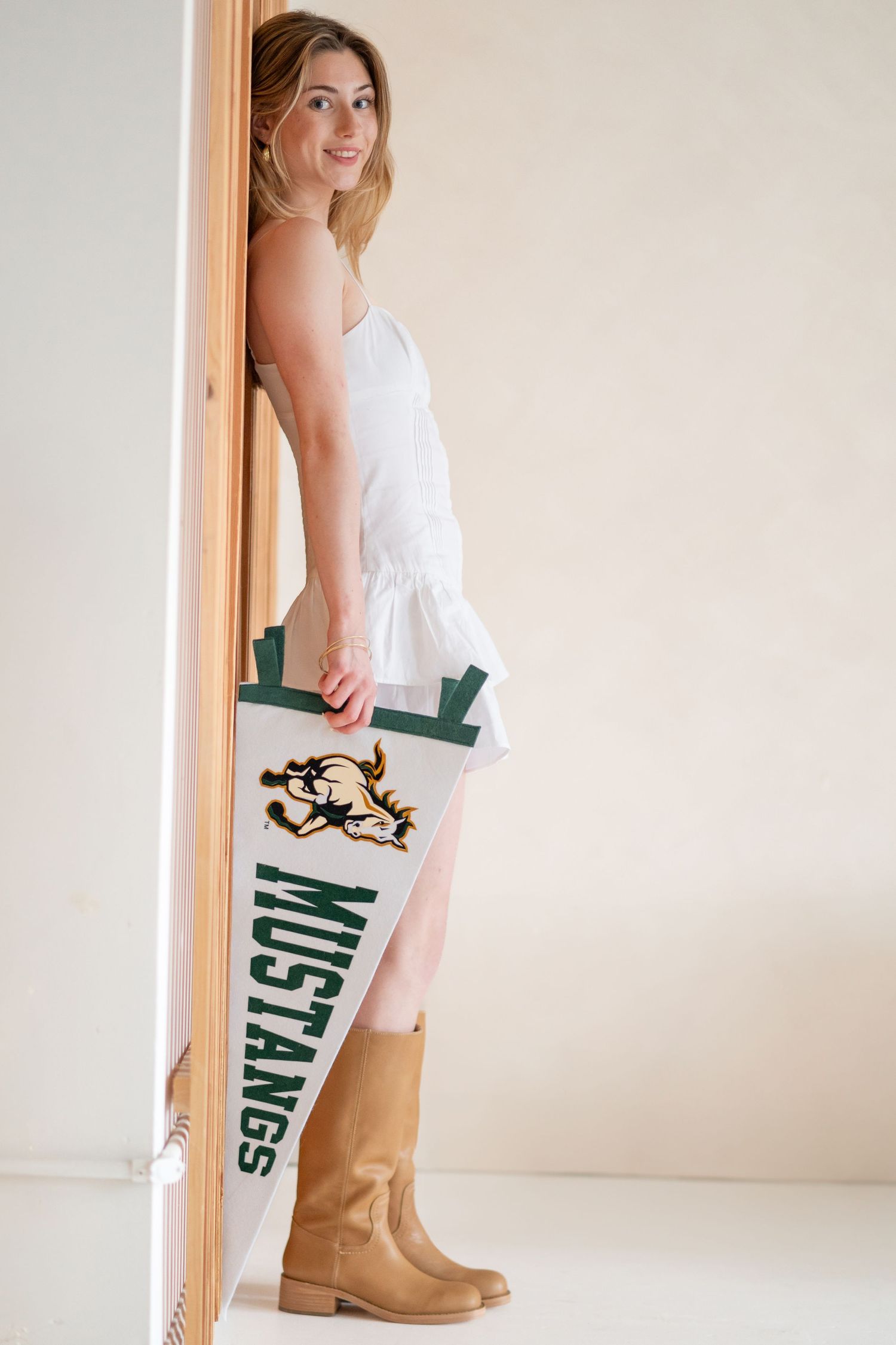 Person in white dress holding collegiate pennant flag and wearing tan boots.