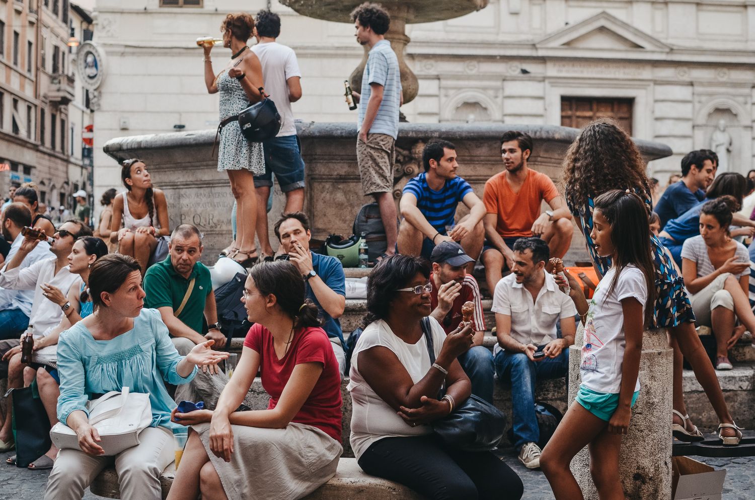 Crowd of people gathered on historic stone steps in a European city square.