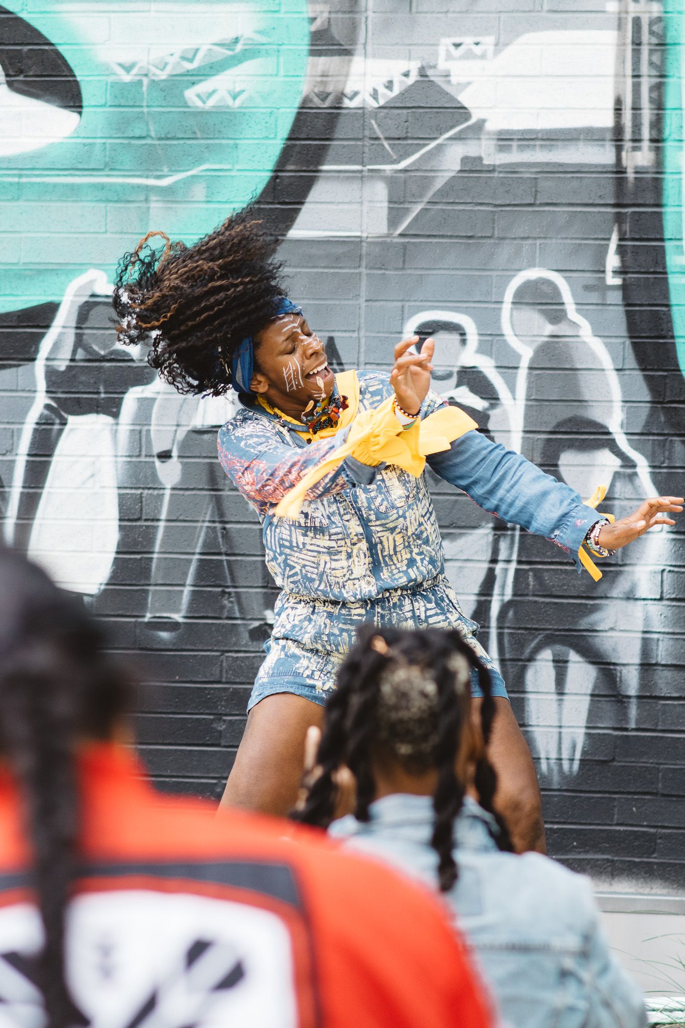 Dancers perform in front of colorful graffiti wall with turquoise background.