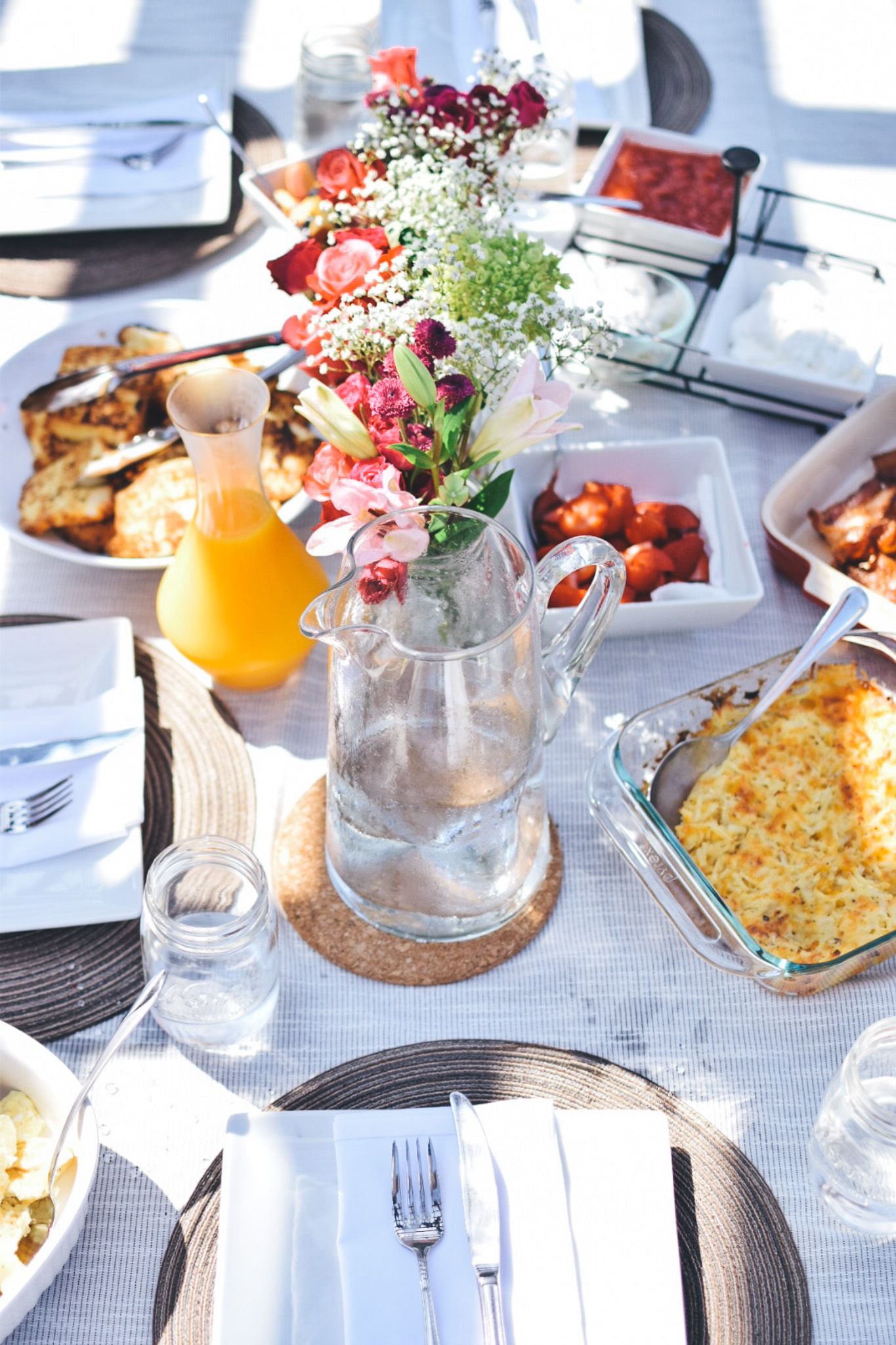 Brunch table spread with colorful dishes, orange juice, and delicate flower arrangements.