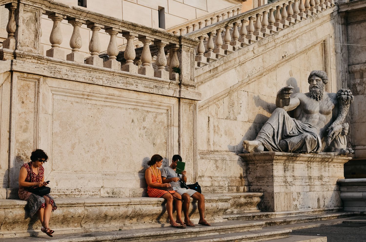People resting on ornate stone steps next to classical statues and architecture.