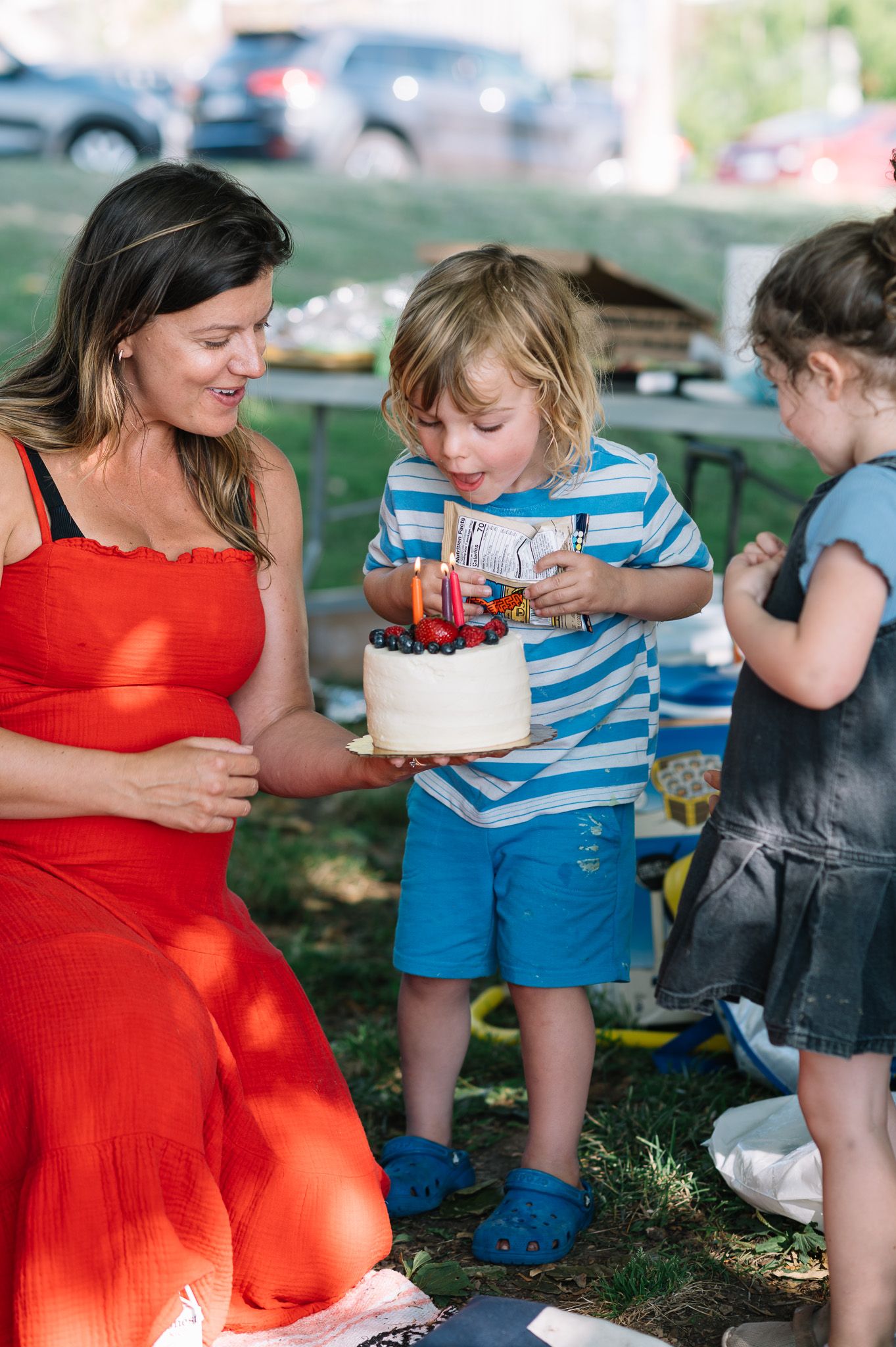 Outdoor gathering with children and adults sharing cake at a summer celebration.