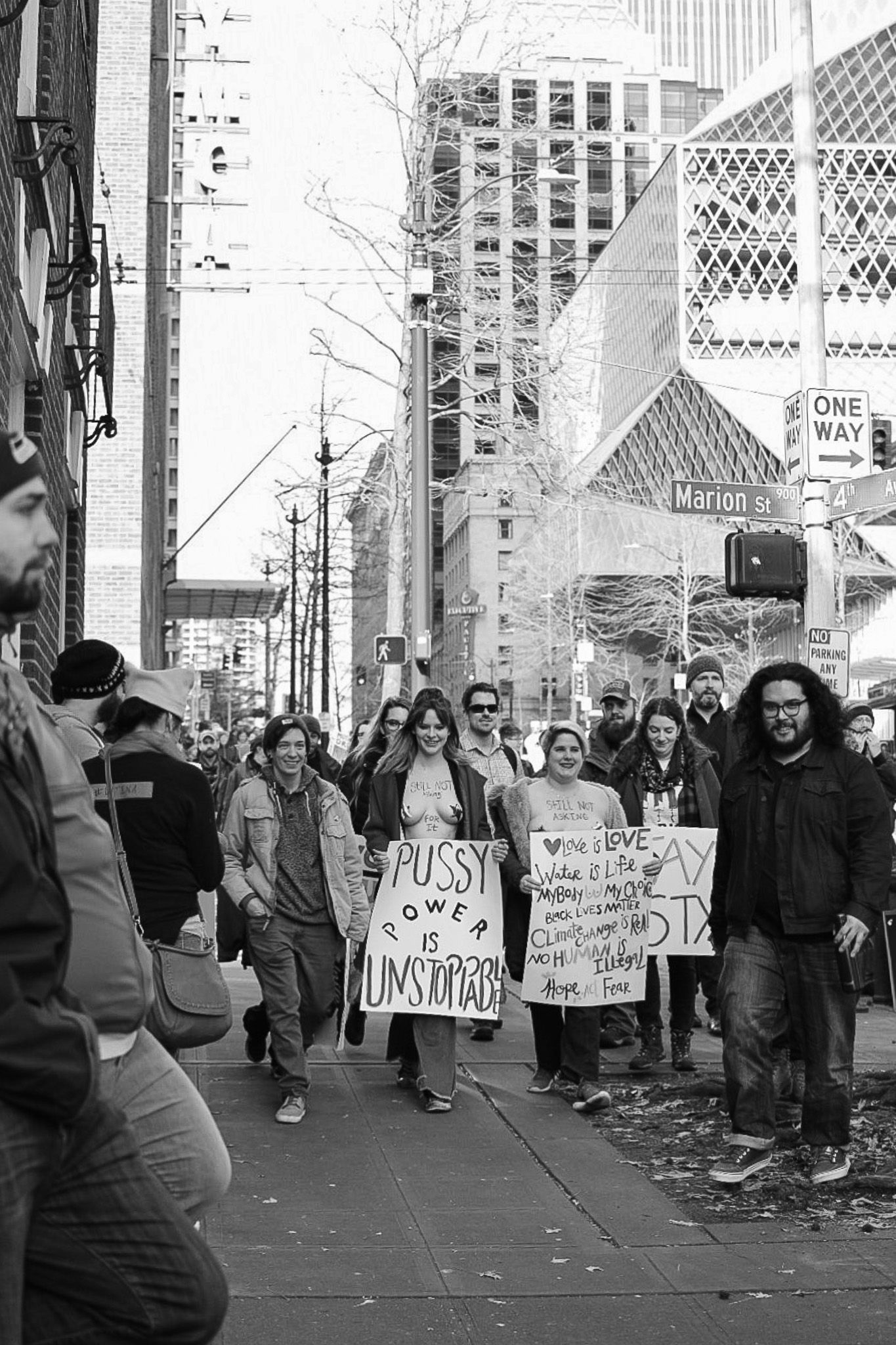 Black and white image of protesters holding signs on a city sidewalk during a demonstration.