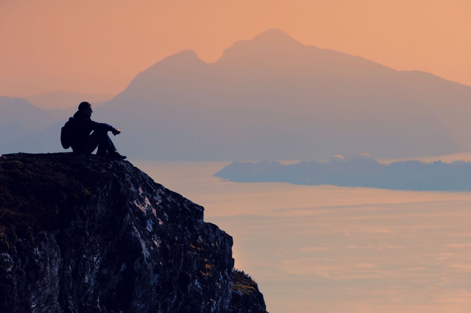 Stemningsfull silhuett av en person som skuer utover norske fjorder og fjell i Bergen. Kunstnerisk landskapsfotografering.