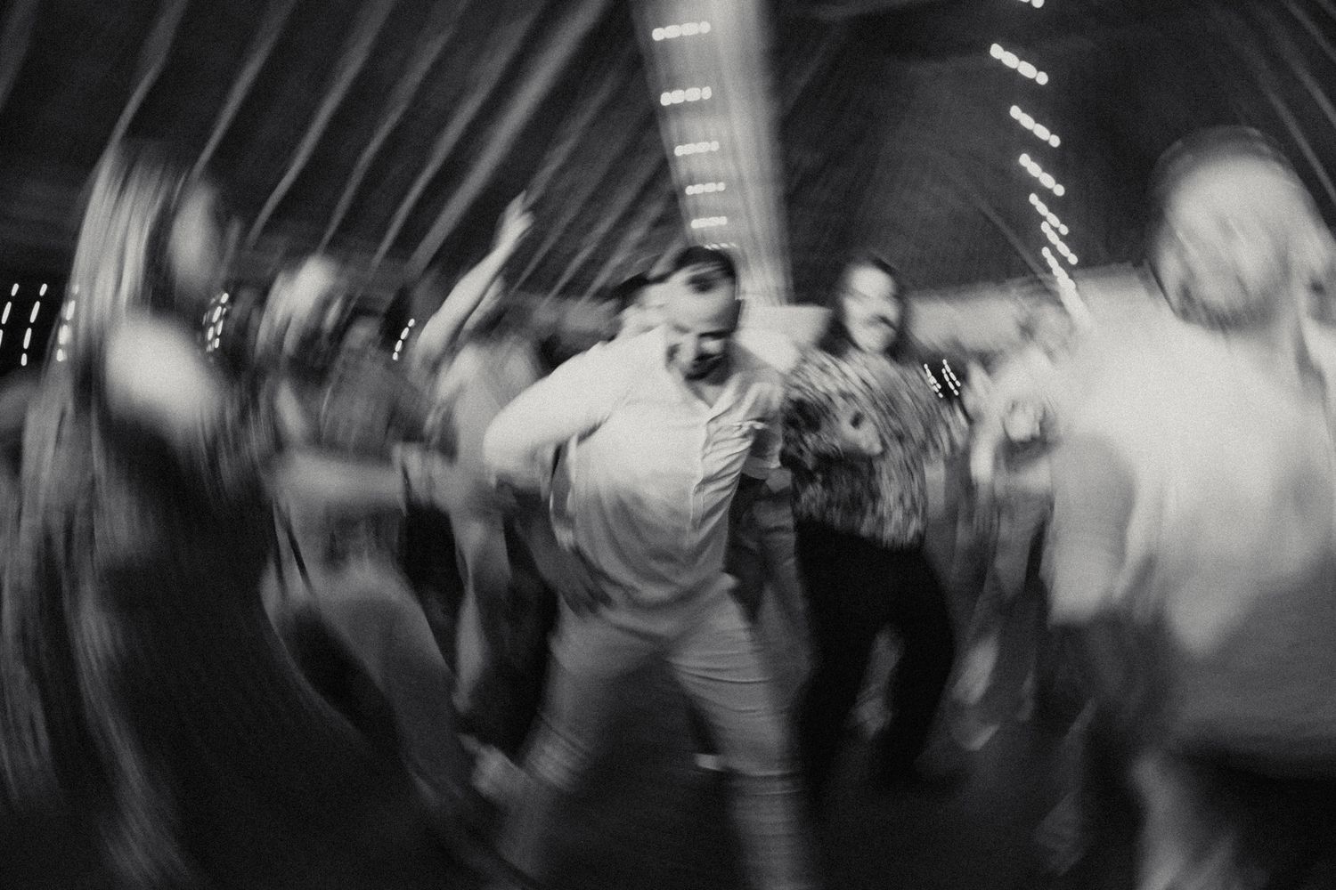 Energetic blurred black and white photo of guests dancing at a lively wedding reception.