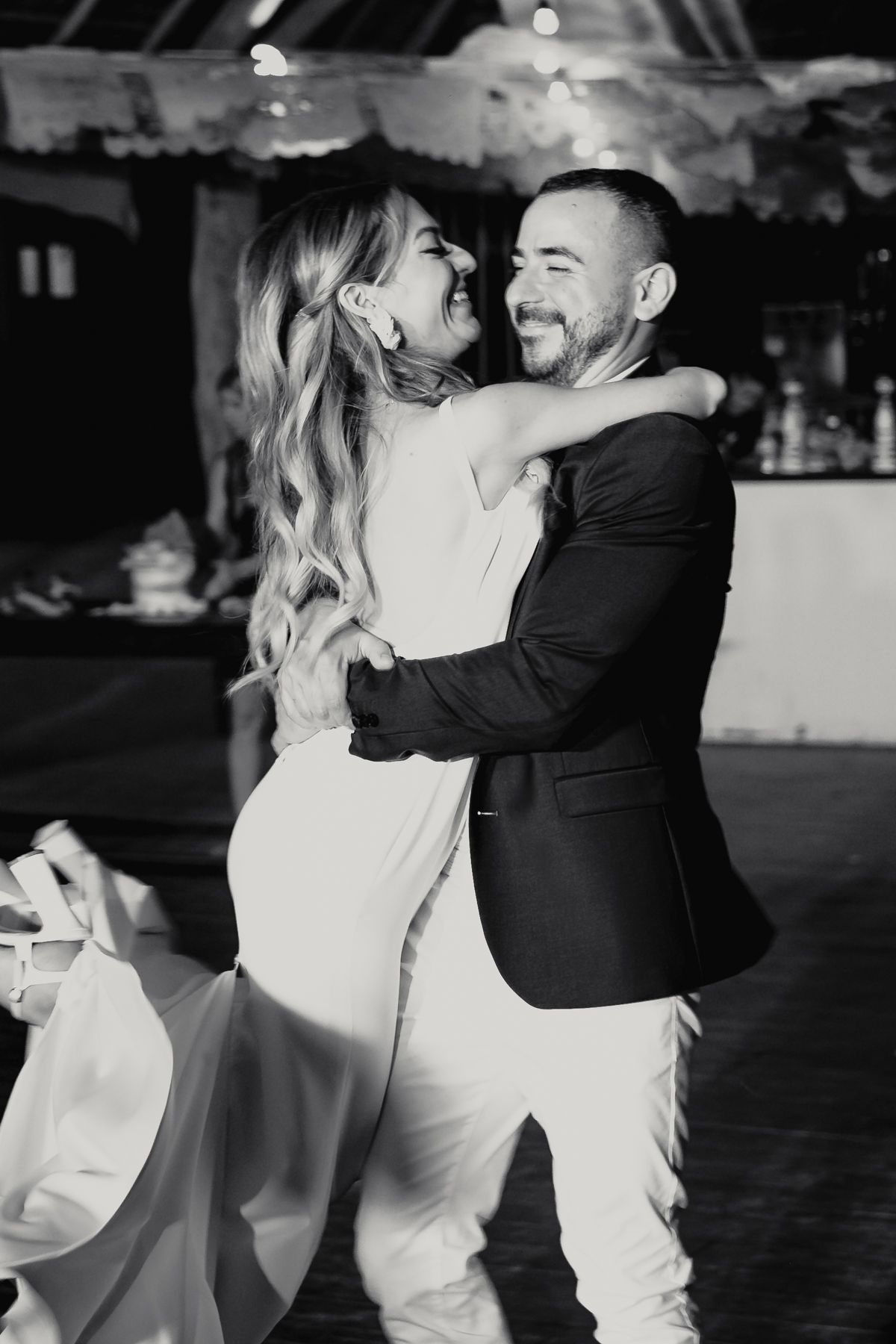 Bride and groom sharing joyful first dance embrace in black and white wedding photo.