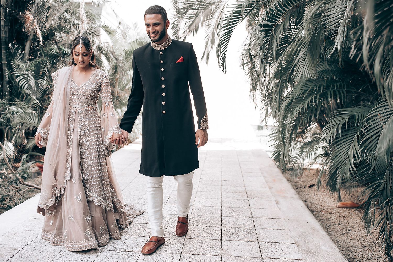 Couple walking along a palm-lined pathway in formal attire.