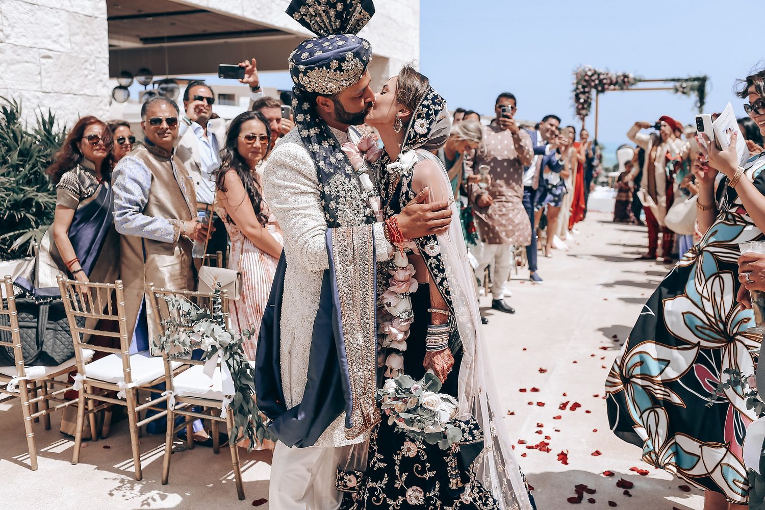 Wedding celebration with guests throwing petals along a white-walled venue.