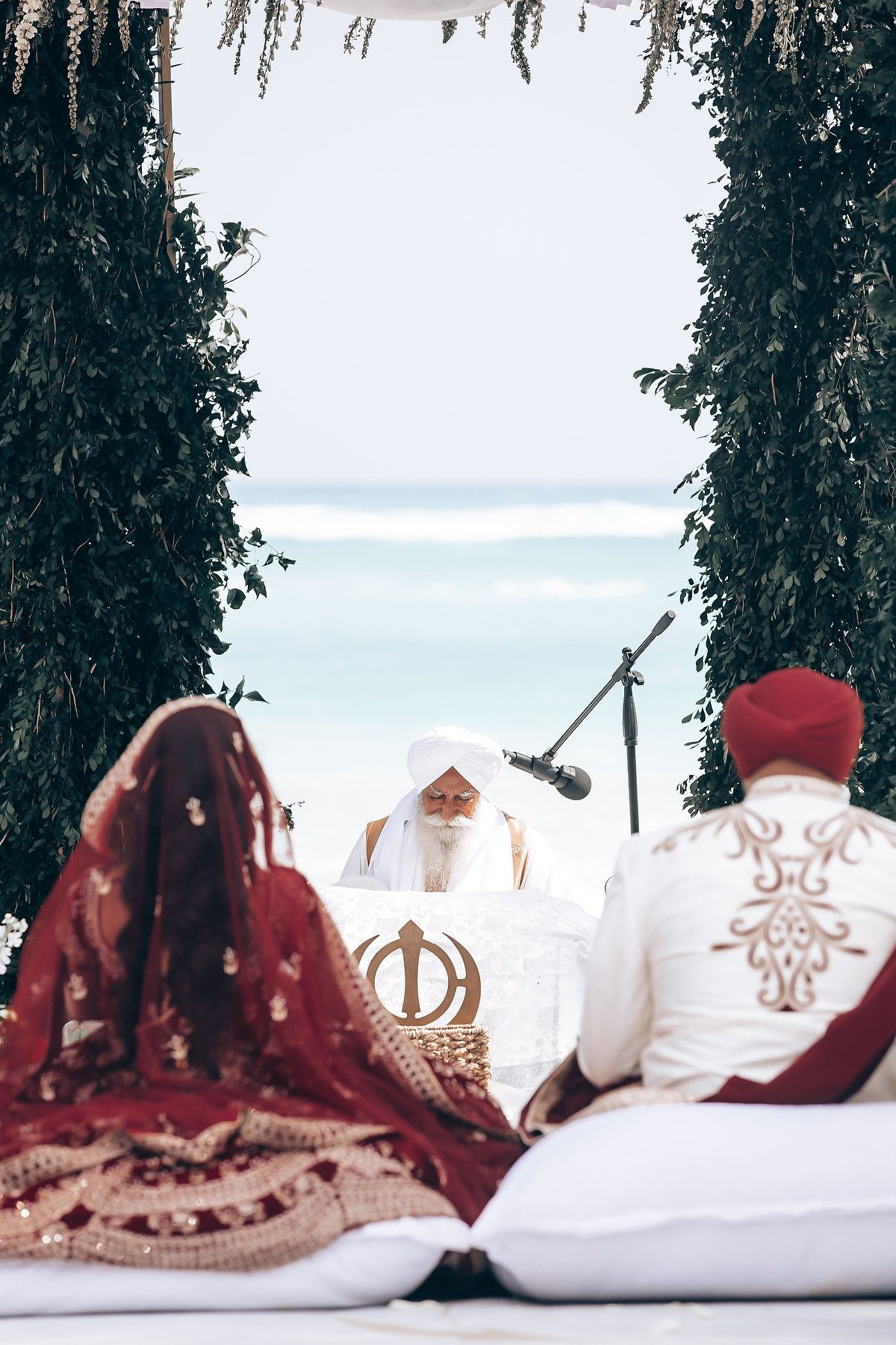 Elegant beachside wedding ceremony with burgundy and white decor against ocean backdrop.