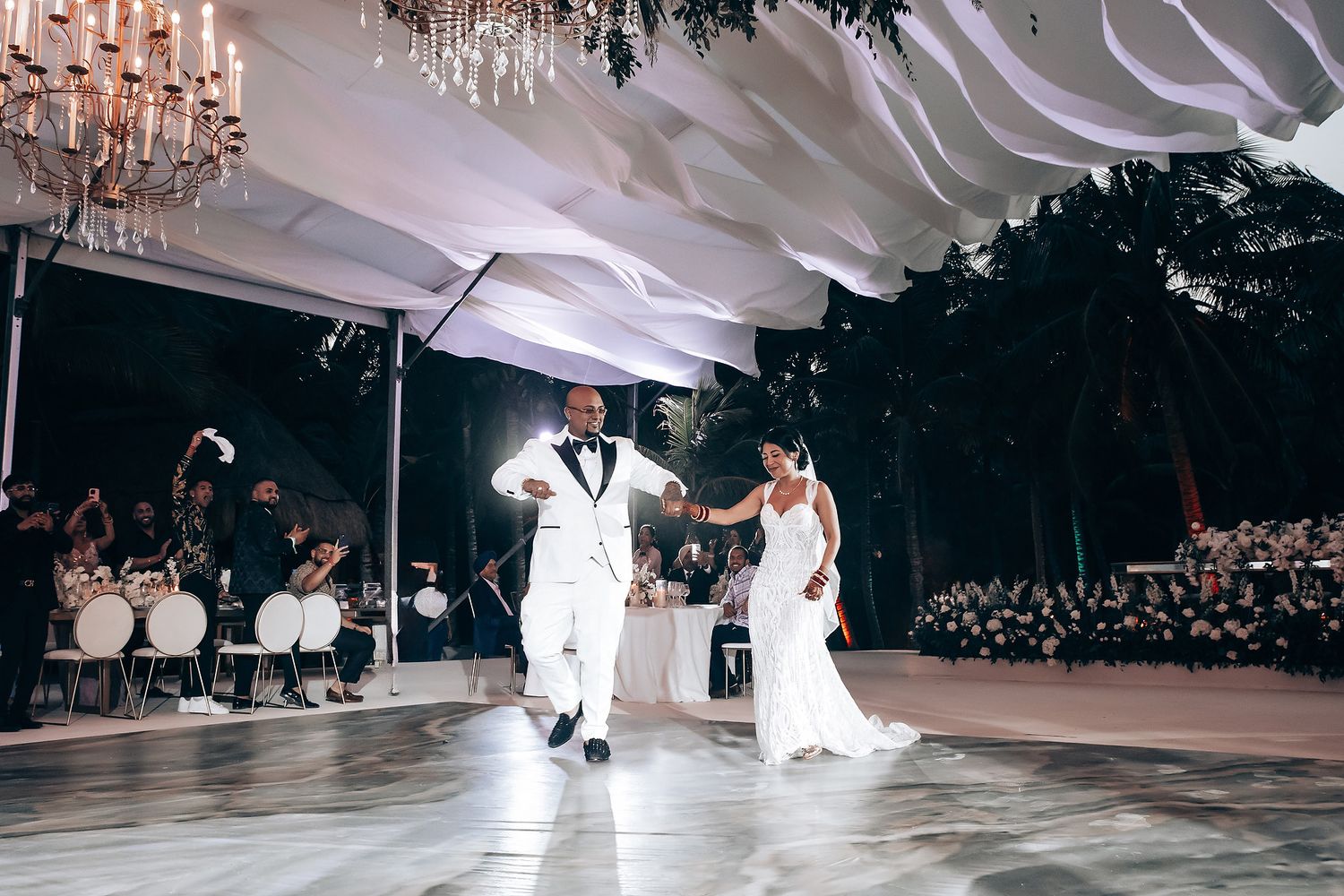Wedding dance celebration under elegant white draping and crystal chandeliers.