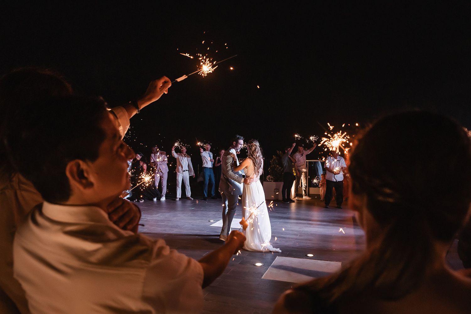 Wedding guests hold sparklers creating a magical nighttime atmosphere during celebrations.