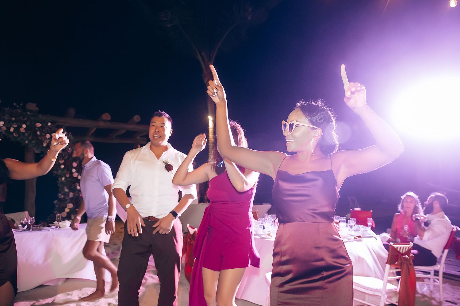 People dancing and celebrating at a nighttime outdoor party with purple stage lighting.