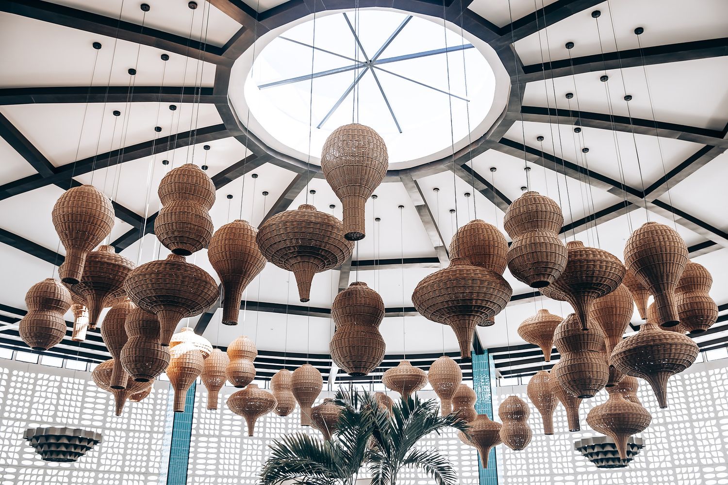 Modern restaurant interior with geometric skylight ceiling and hanging woven rattan pendant lights creating an airy atmosphere.
