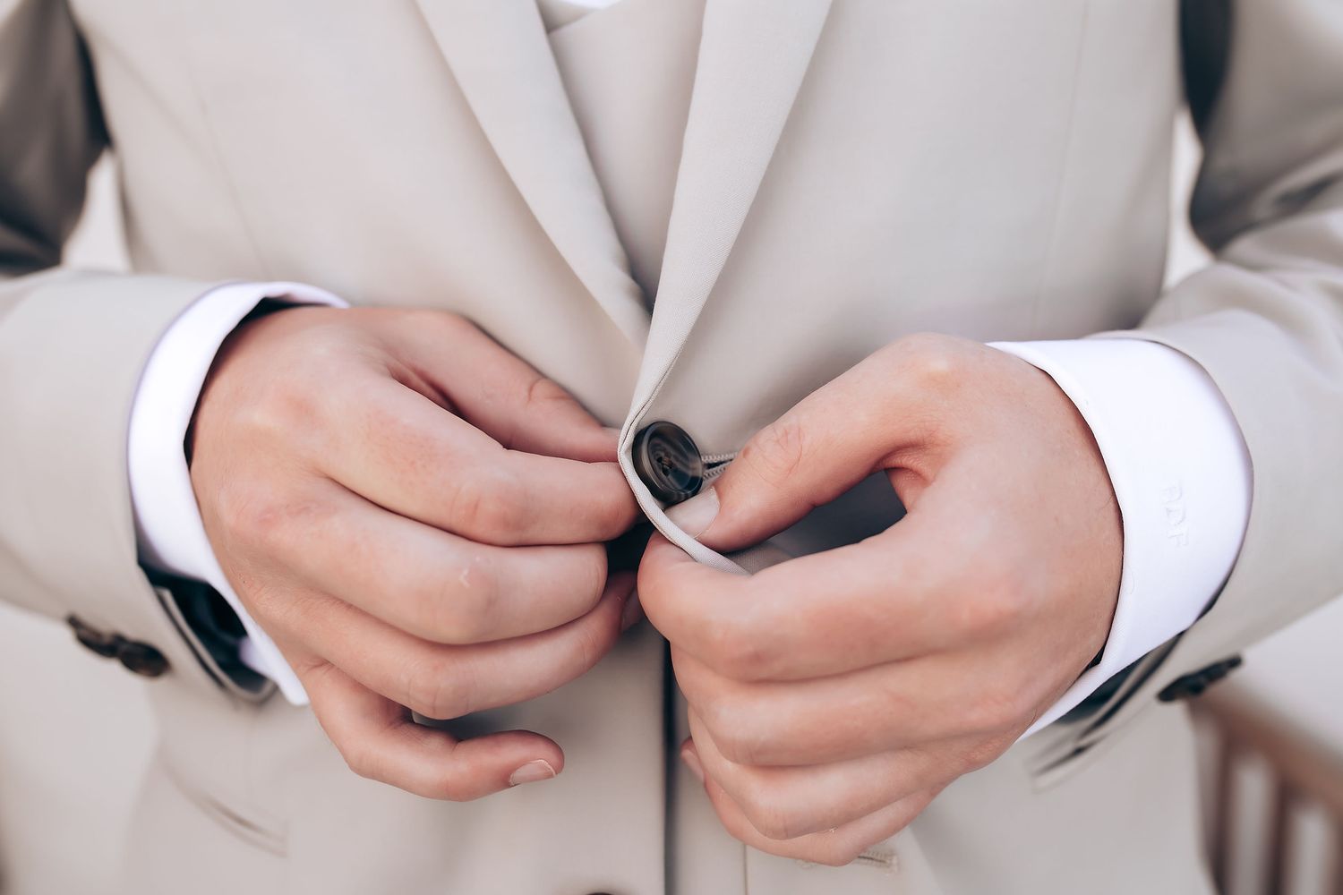 Close-up details of a light gray suit jacket with buttons being adjusted.