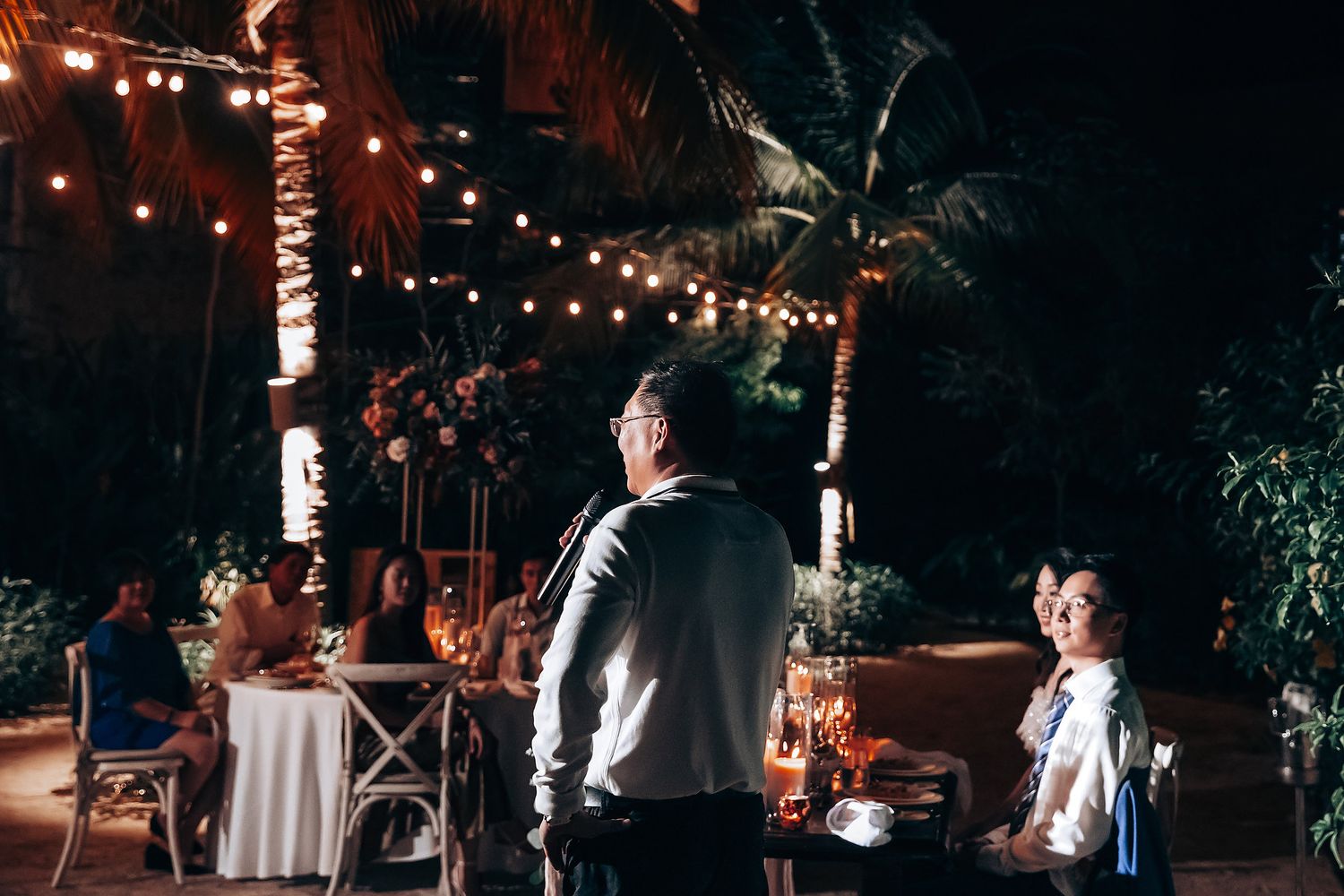 Evening outdoor reception with string lights illuminating palm trees.