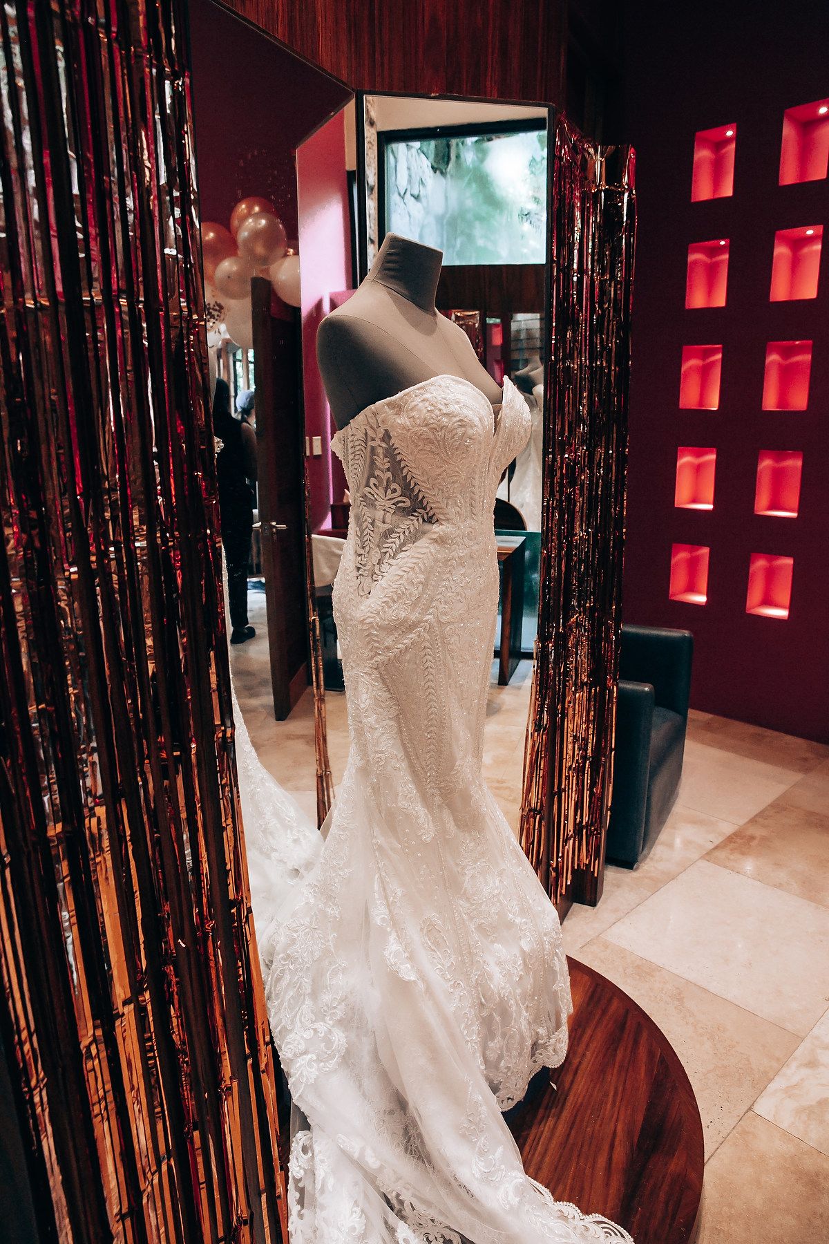 Elegant lace wedding dress displayed in a boutique with dramatic red lighting and black curtains.