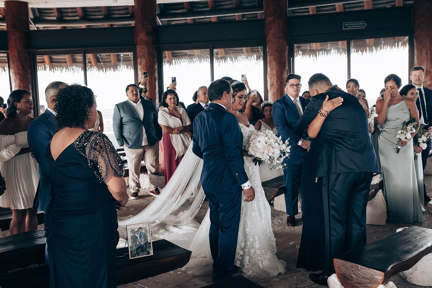 Wedding guests gather in a thatched-roof venue during an intimate celebration with formal attire.