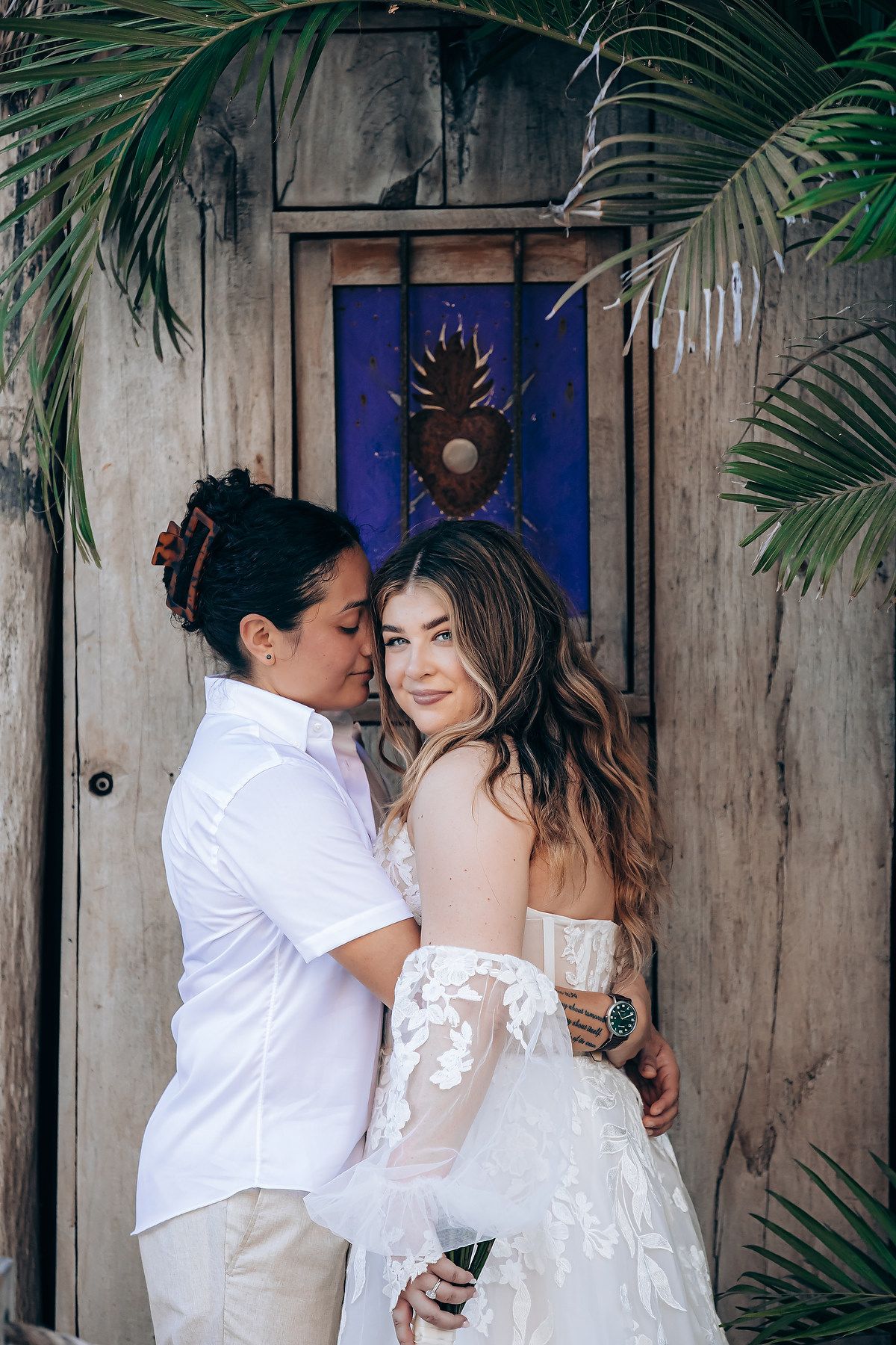 Intimate moments captured against rustic wooden walls with tropical palm fronds.