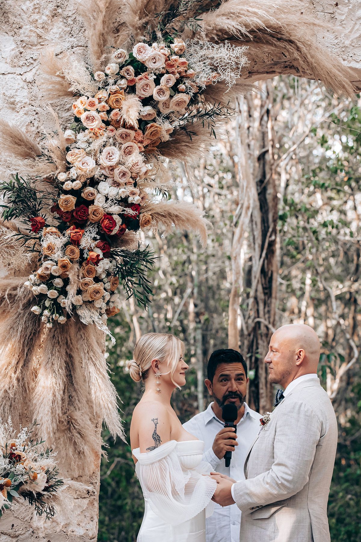 Outdoor wedding ceremony setup with pampas grass and floral arch in a natural forest setting.