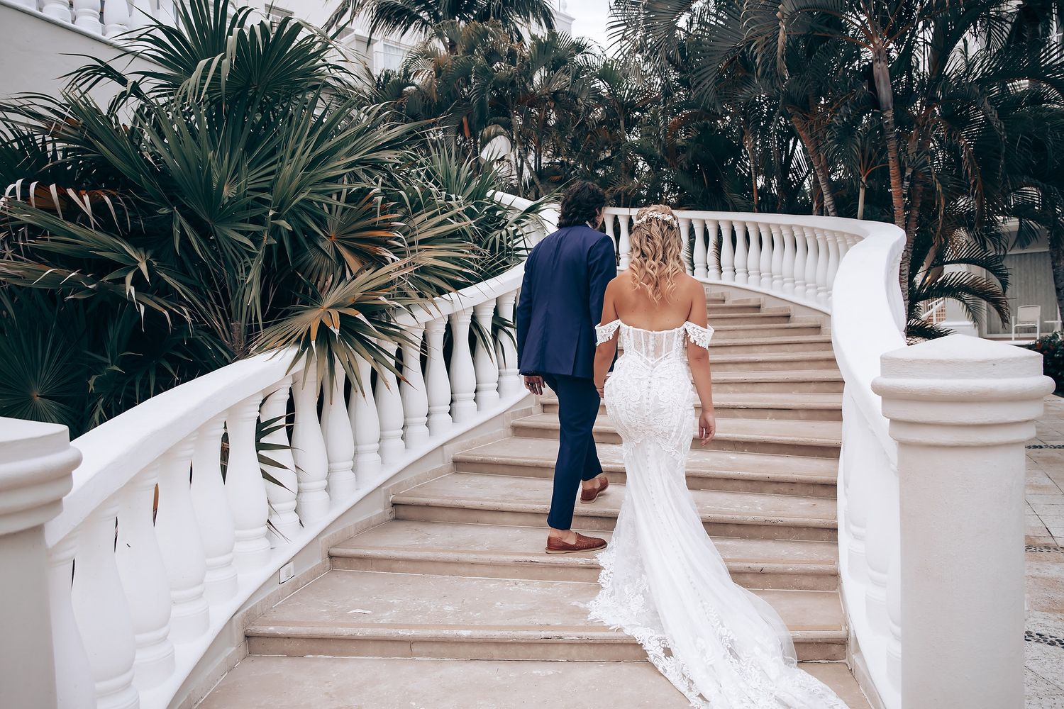Wedding couple walking up elegant white stone stairs surrounded by tropical landscaping.