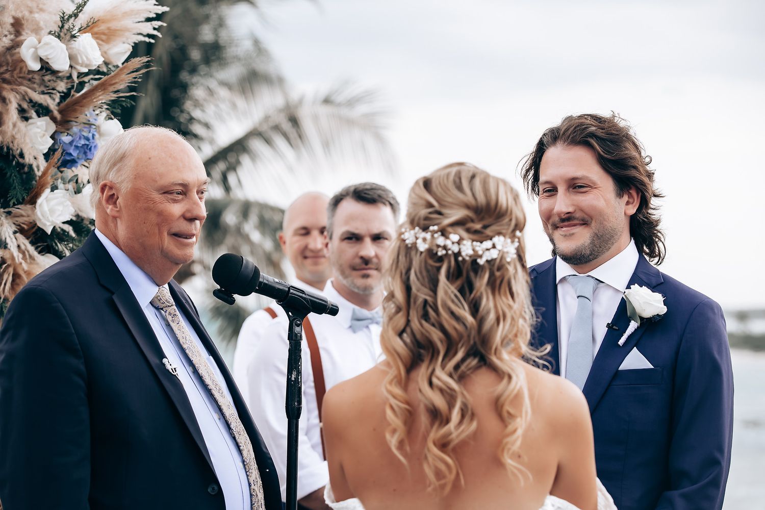 Elegant outdoor wedding ceremony with guests seated in white chairs by the ocean.