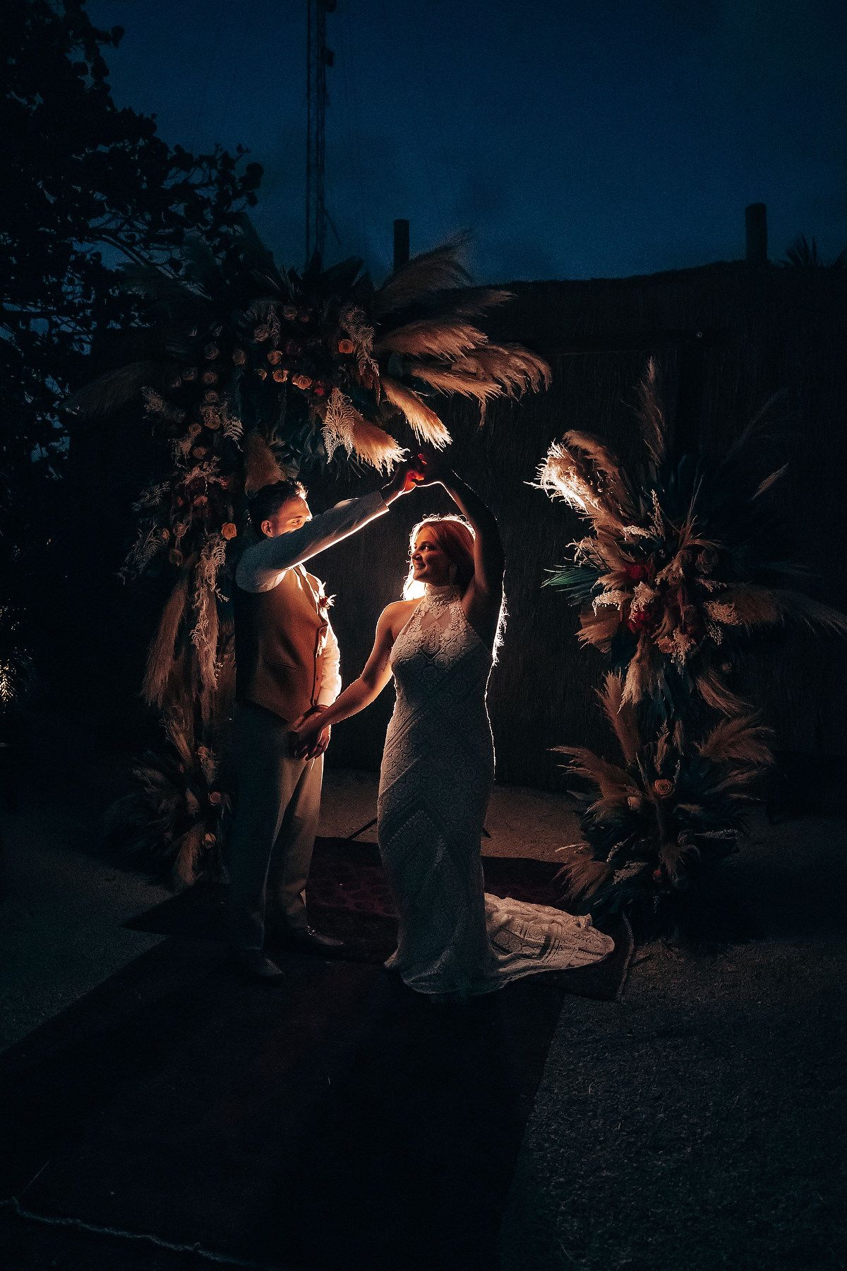 A romantic nighttime scene illuminated by spotlights under palm trees creating a dramatic tropical atmosphere.