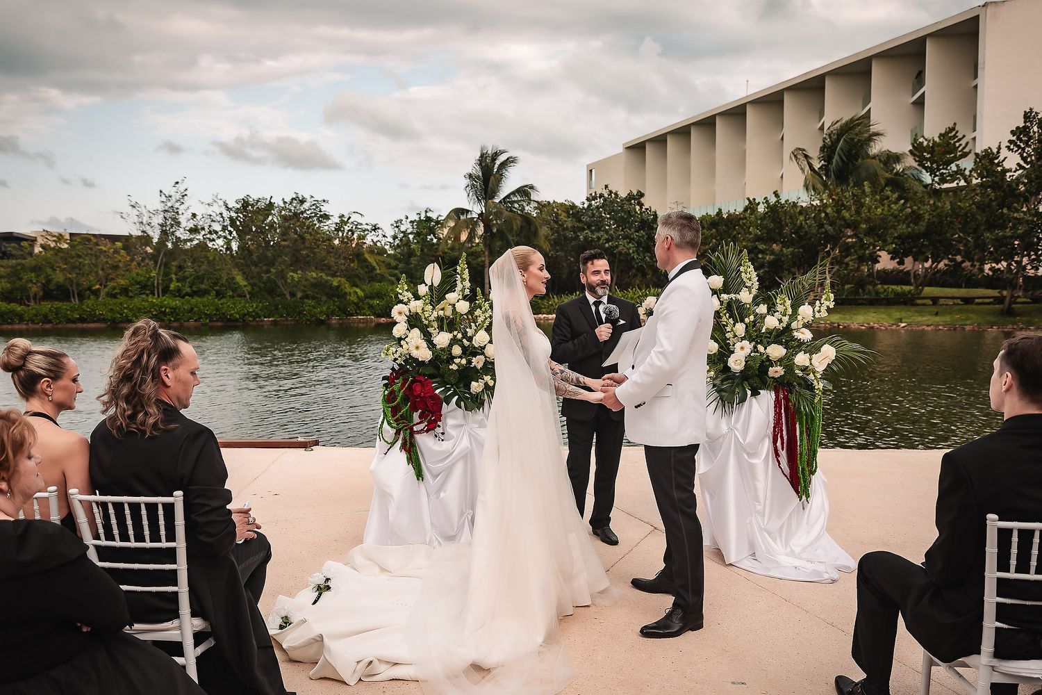 Outdoor wedding ceremony setup with white chairs and floral arrangements by the water.