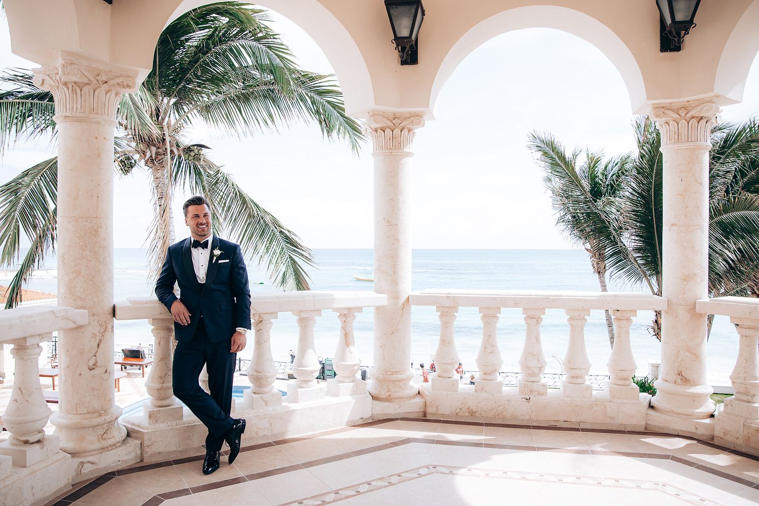 A Mediterranean-style colonnade with white arches and balustrades overlooking a beachfront setting.