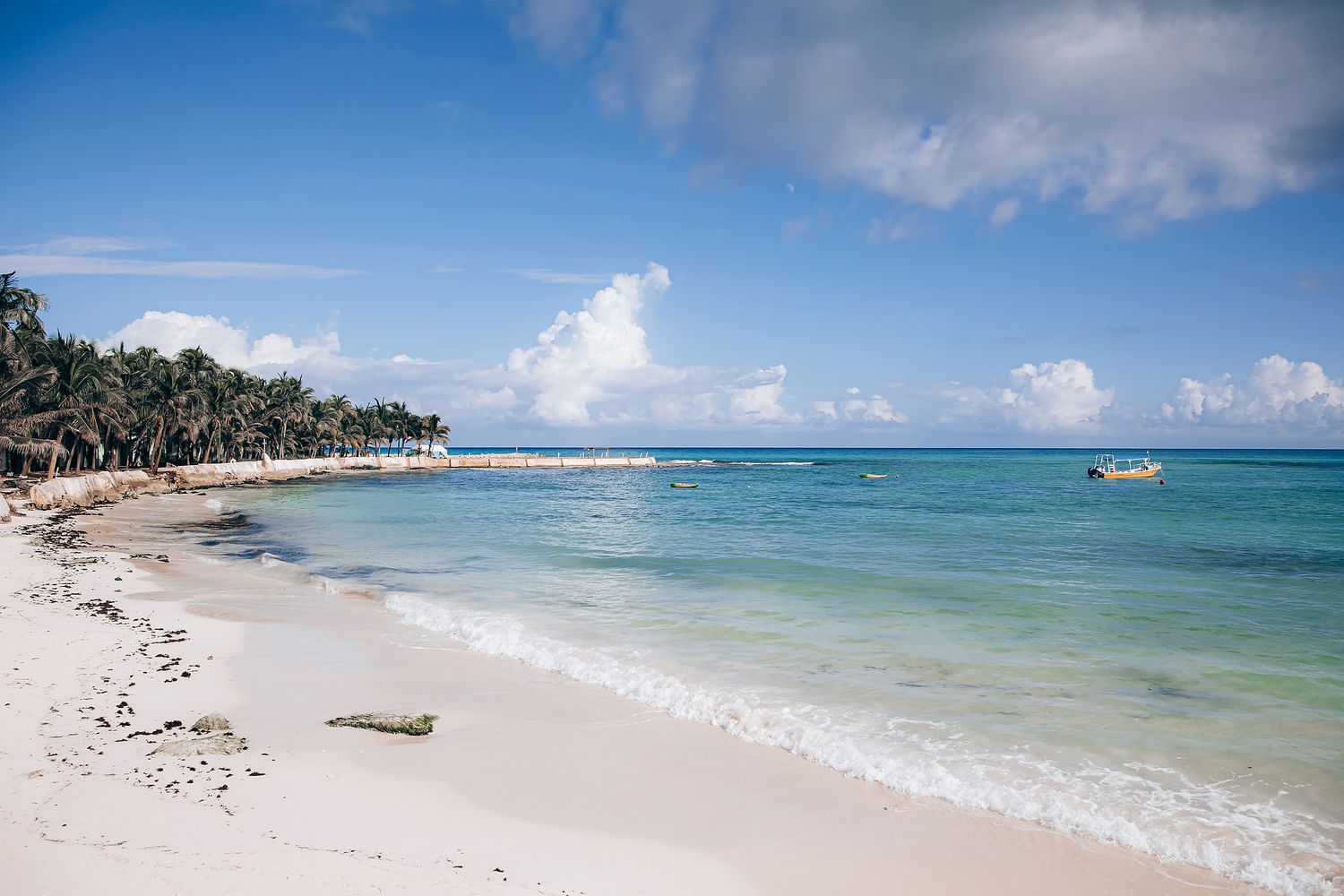 Stunning tropical beach panorama with turquoise waters, white sand and palm trees along the shoreline.
