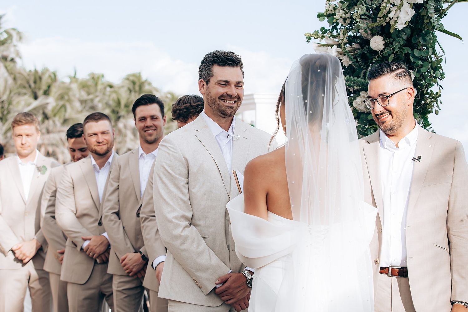 Wedding party members in beige suits gather together for group photos during an outdoor celebration.