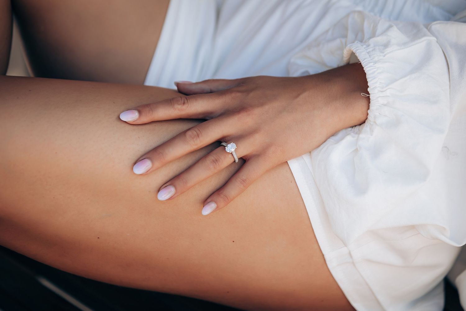 Close-up view of a sparkling engagement ring on a woman's hand against a white background.