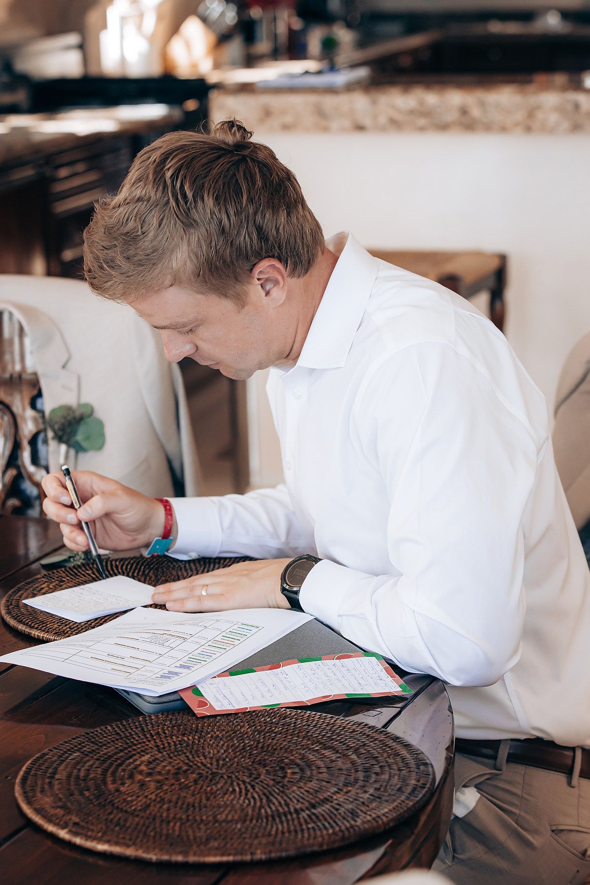Student in white shirt writing in notebook at wooden table with woven placemat, viewed from multiple angles.