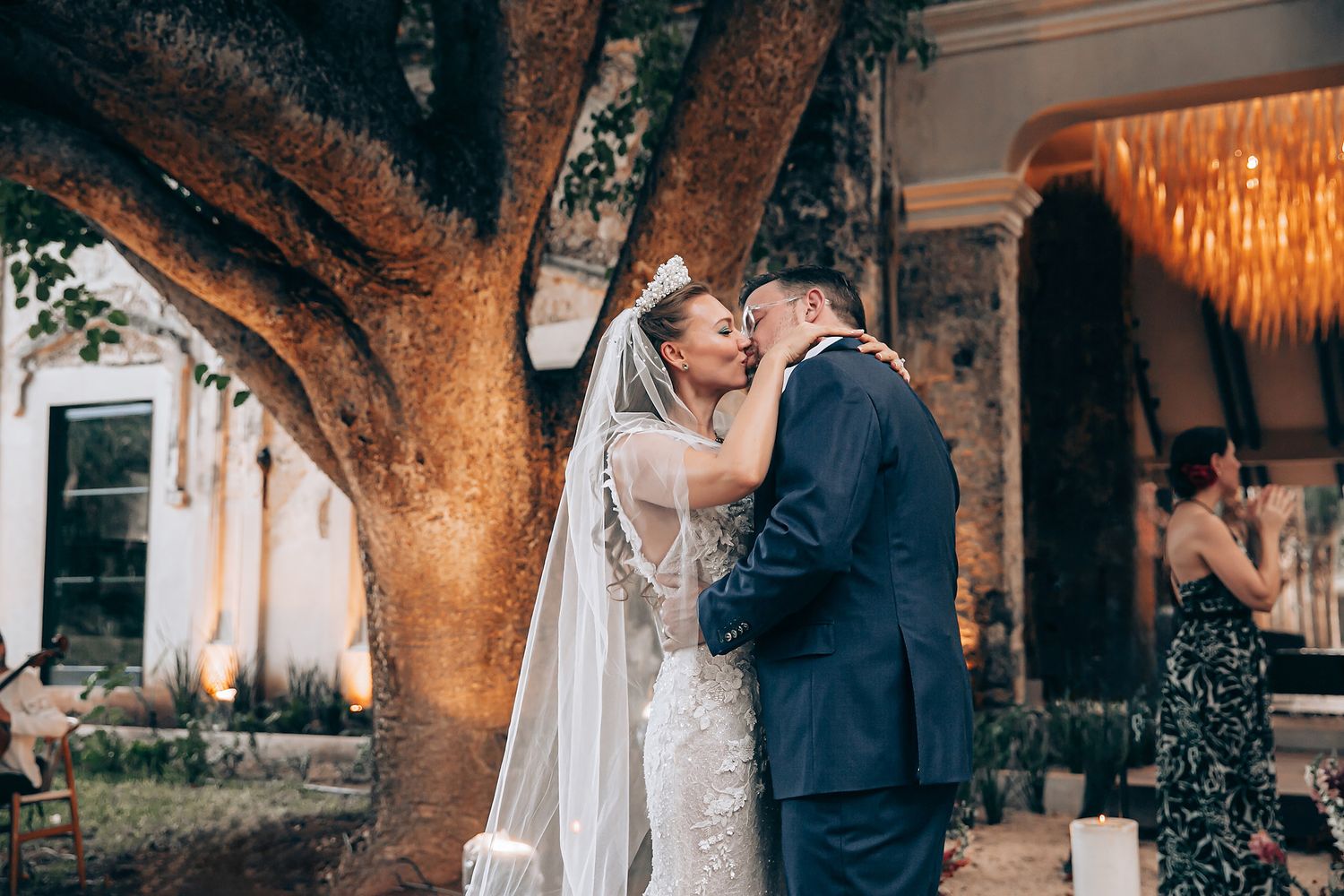A romantic couple shares intimate moments in an outdoor garden setting with string lights and trees creating a magical atmosphere.