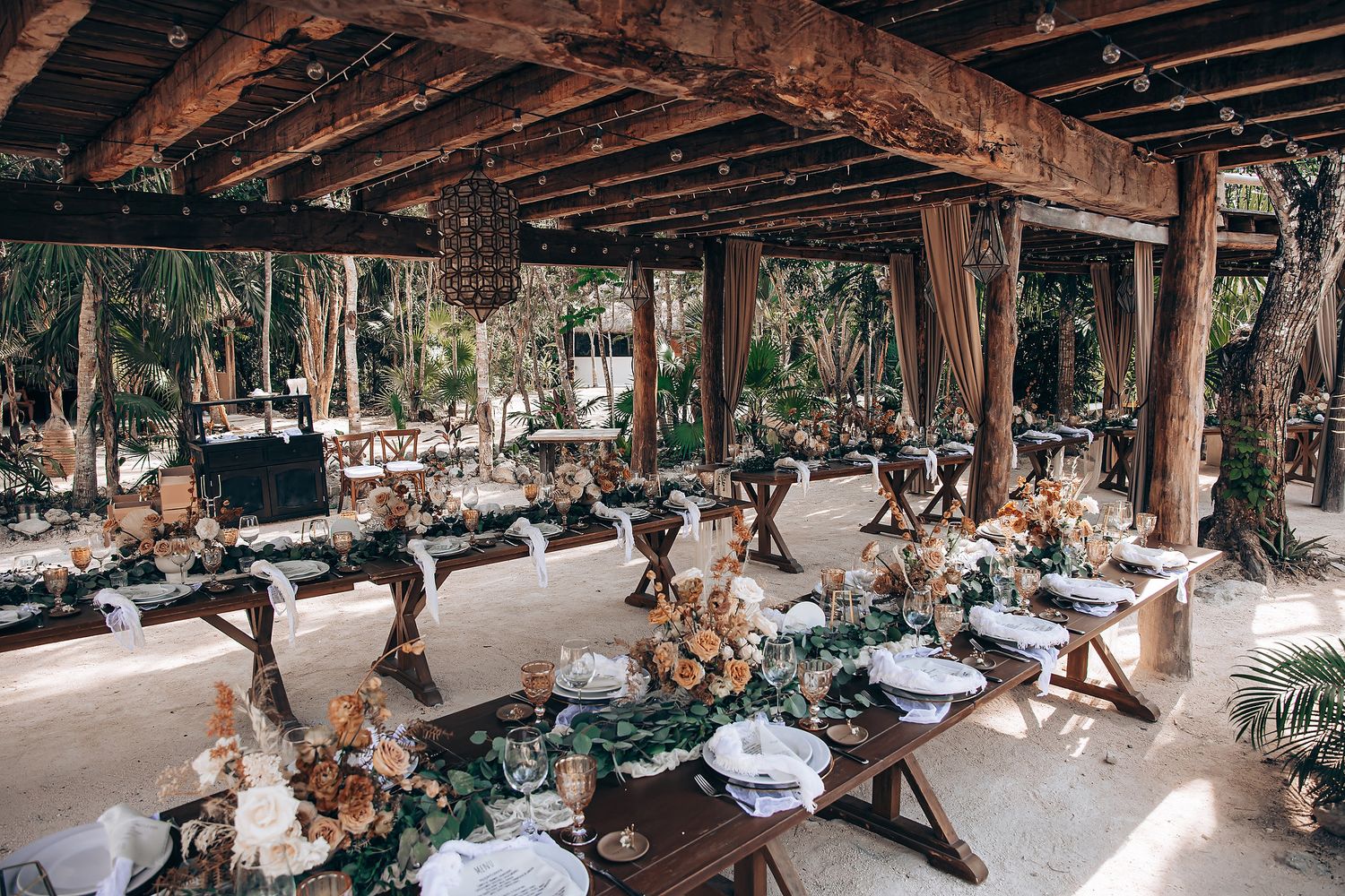 Panoramic view of an outdoor wedding reception setup with wooden tables and natural decor.