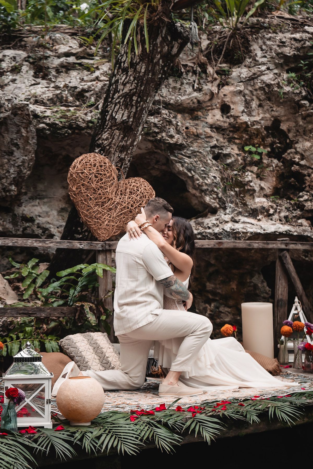 Romantic picnic setup with heart decor and lanterns by a rocky cave wall.
