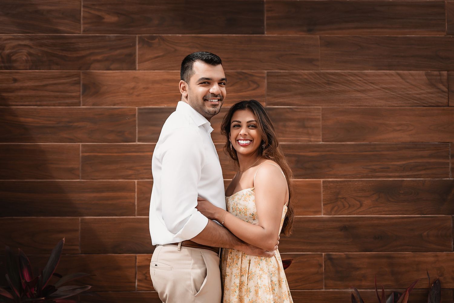 Couple laughing together against dark wooden wall during engagement session.