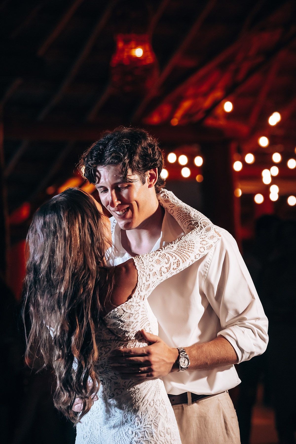 Couple sharing a romantic dance moment under red mood lighting at their wedding reception.