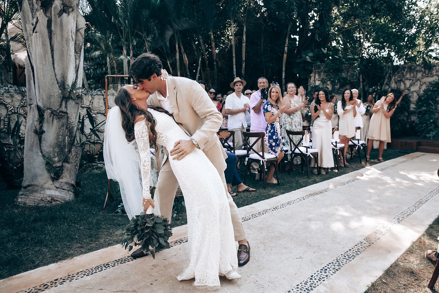 Outdoor wedding celebration with guests seated along a decorated pathway.