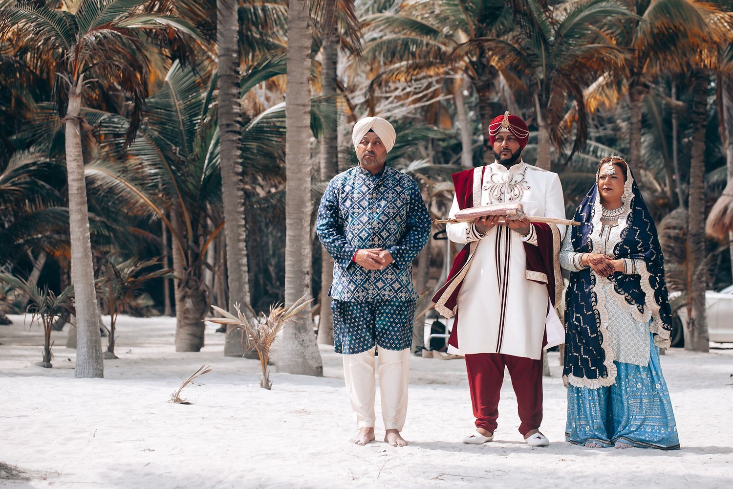 Traditional Indian wedding ceremony procession with guests walking through a palm tree lined path on a beach.