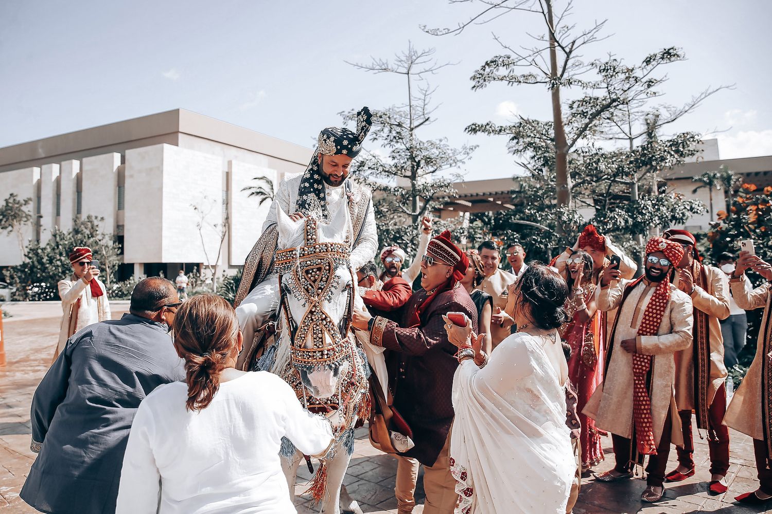 Celebratory outdoor wedding scene with traditional cultural attire and guests gathered around in a joyful moment.