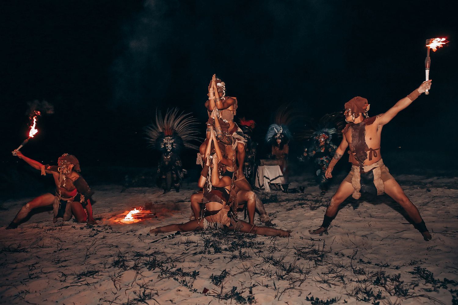 Performers spin fire torches in synchronized movements during a dramatic beach fire dance show at night.